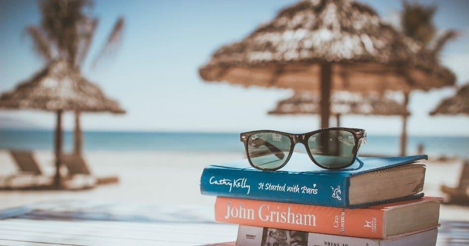 Three books and a pair of glasses on a beach